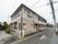 白とグレーを基調とした２階建てのアパートが立っている。車道から玄関までは緩やかなスロープになっている。