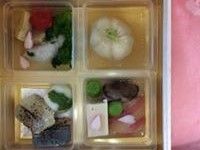十字に仕切られた入れ物に、煮物や焼き物などが見栄え良く入っている。春らしく桜の花びらがあしらわれている。