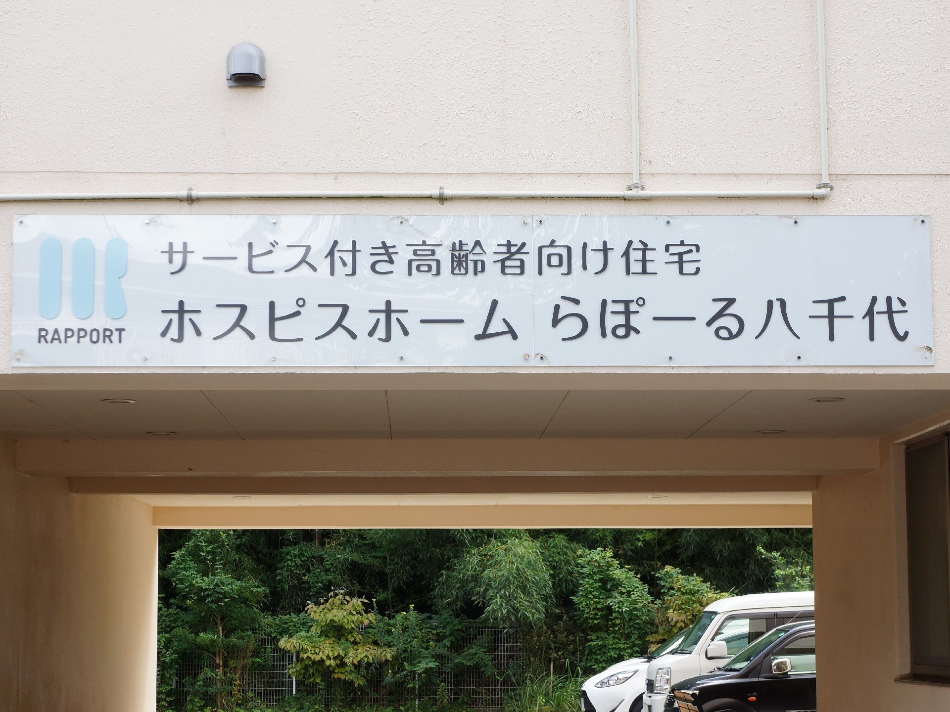 駐車場に入る入口の上方に掲げられた、細長いホームの看板