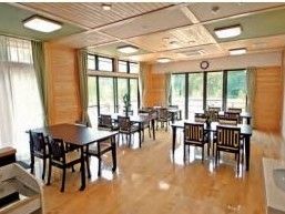 天井、壁、床ともに木目の美しい、広いリビング。たくさんの大きな窓があり、明るく開放的である。椅子が４脚置かれた机が５台並んでいる。