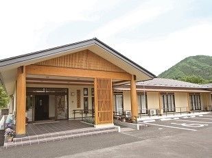 リゾート施設のような平屋の建物。玄関前にはスロープがついており、駐車場も整備されている。周囲には緑豊かな山が望める。