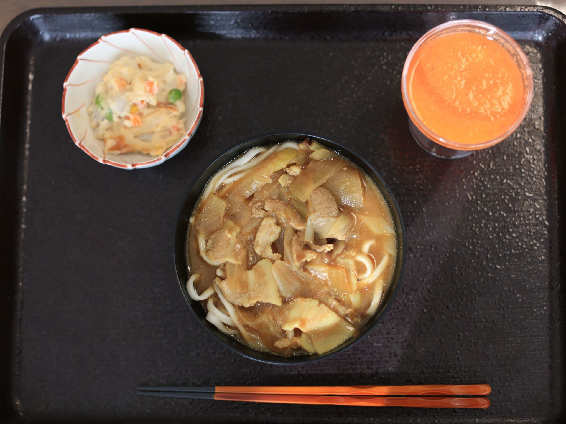 食事は毎食、１人ずつトレーに乗せられて提供される。食事の一例は、メインにカレーうどん、小鉢にサラダがあり、デザートがついている。