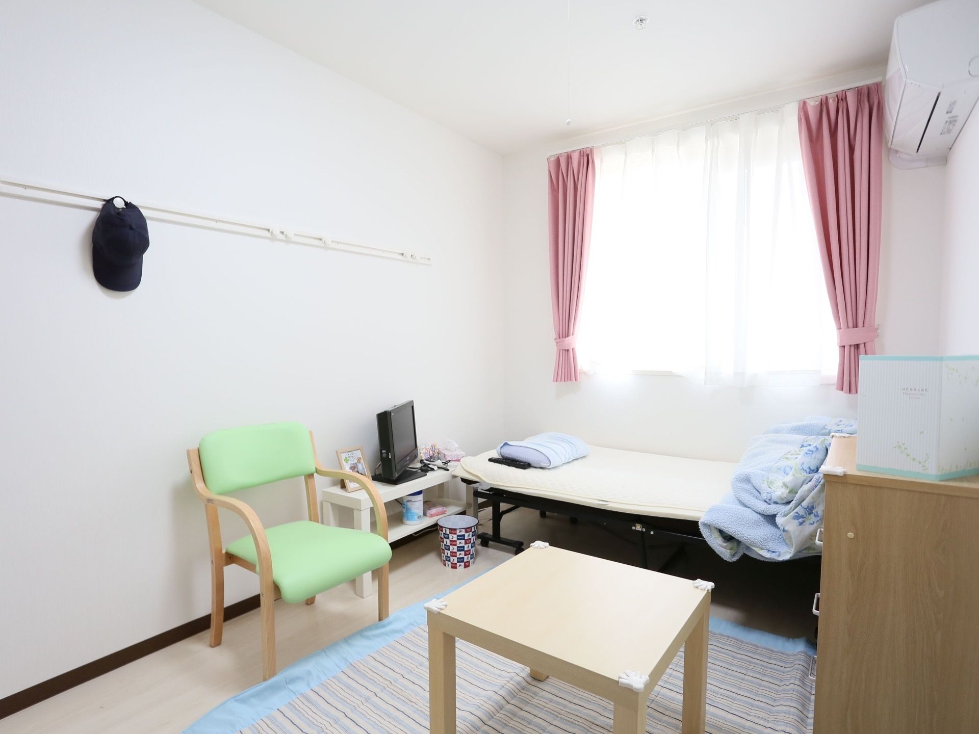白を基調にした明るく爽やかなデザインの居室である。窓際にベッドがあり、部屋の真ん中あたりに四角いテーブルと椅子がある。