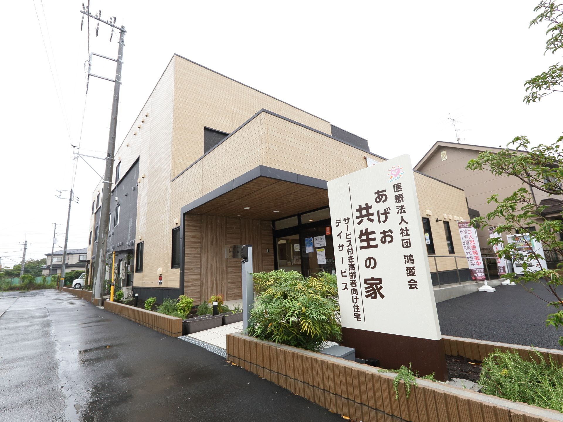 道路と建物の境にはレンガで小さな花壇が作られている。建物の外観はベージュ色と黒くになっている。玄関部分には屋根が付いている。