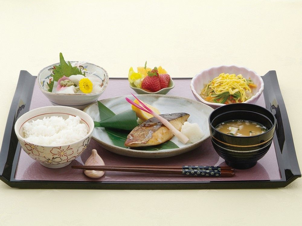 鯖の焼き物とイカの刺身、数種の果物が並ぶ豪華な食事