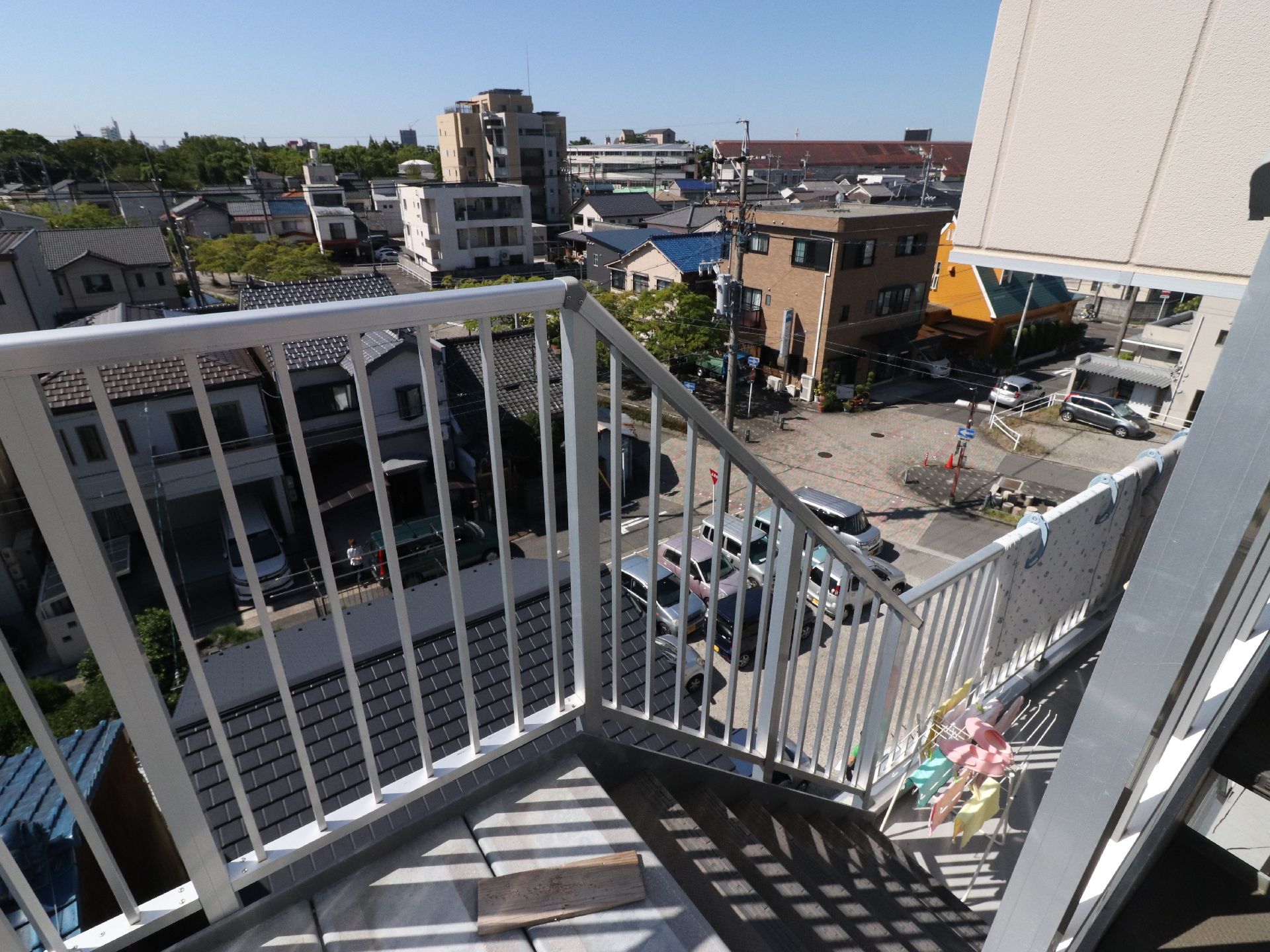階段の下には物干し場があり、黄色、ピンク、グリーンのタオルが干してある。柵の向こうには、一軒家が並んで建っている。