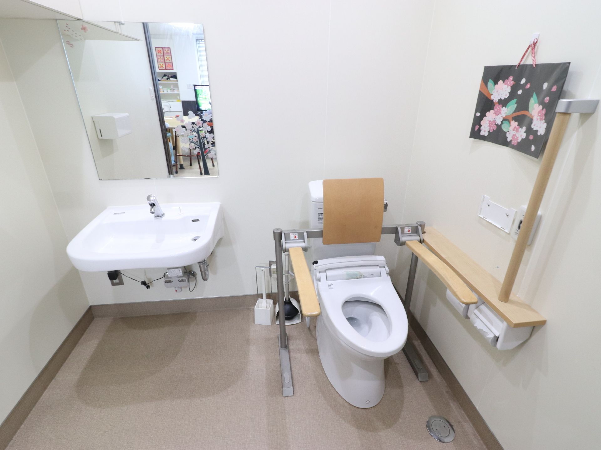 便座には蓋がなく壁には手すりが付けられている。トイレットペーパーが2個セットされている。便座の横に手洗い場があり、足元は空間がある。