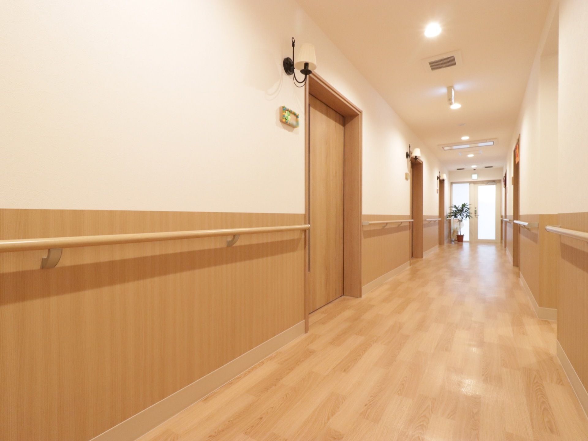 木を基調とした廊下が明るく照らされている。廊下は居室に沿って直線上に伸びており、壁には手すりが設置されている。