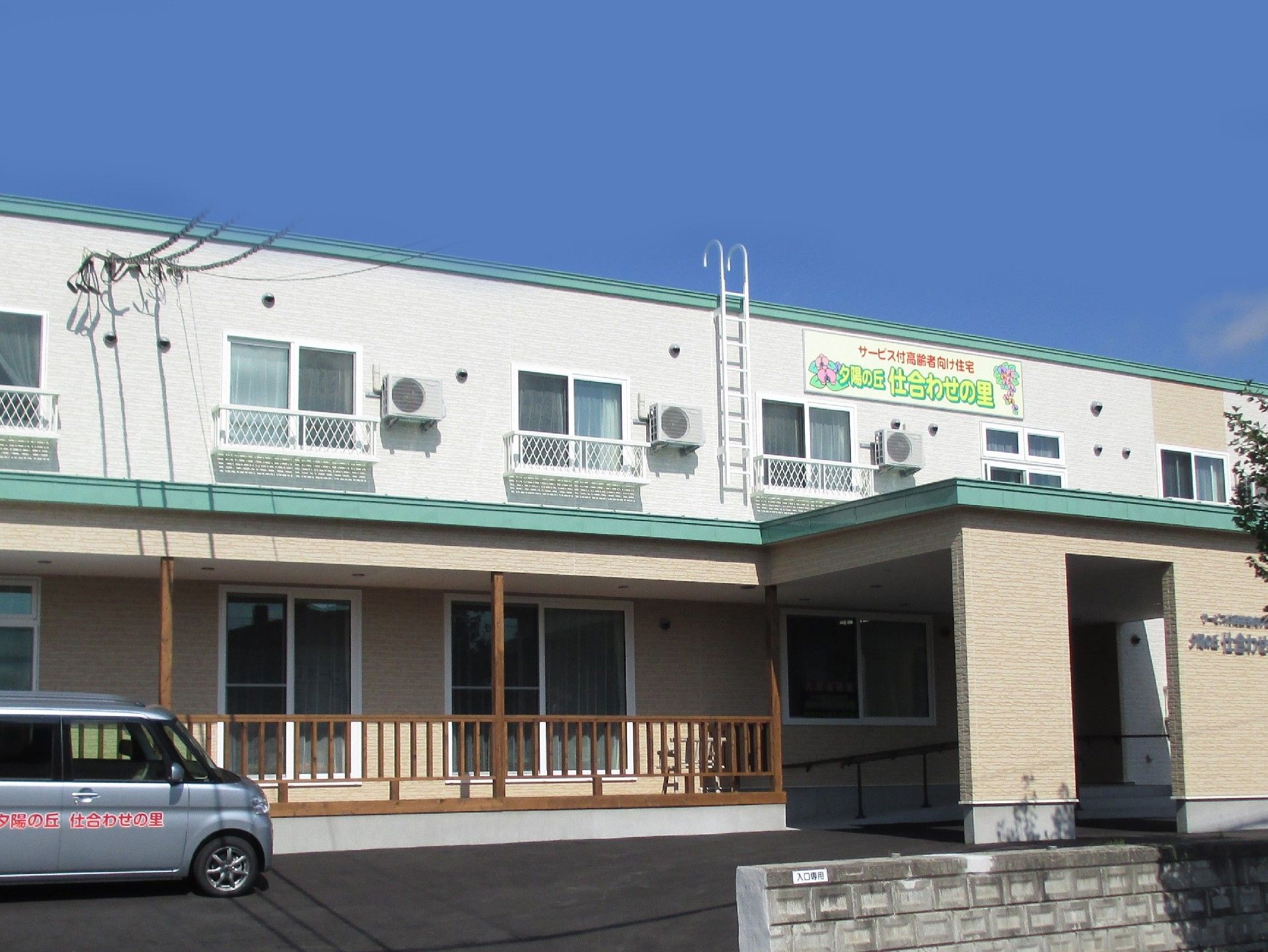 1階はベージュに緑の屋根、2階は白に緑の屋根になっている2階建ての建物