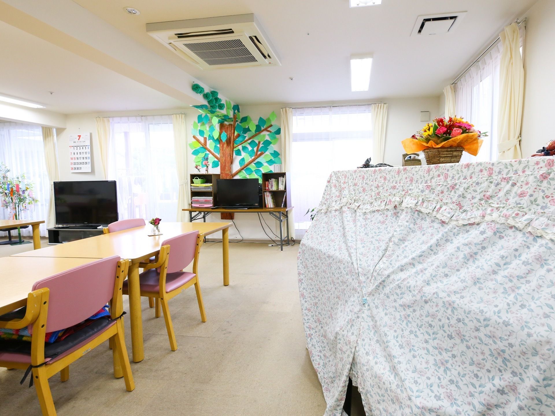 季節感あるレイアウトが工夫されている。テレビや明るい木目調のテーブルセットが設置された共有スペースである。
