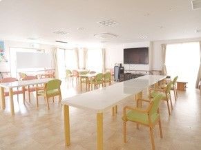 右正面に大型テレビがあり、その両側と左奥に窓のある食堂