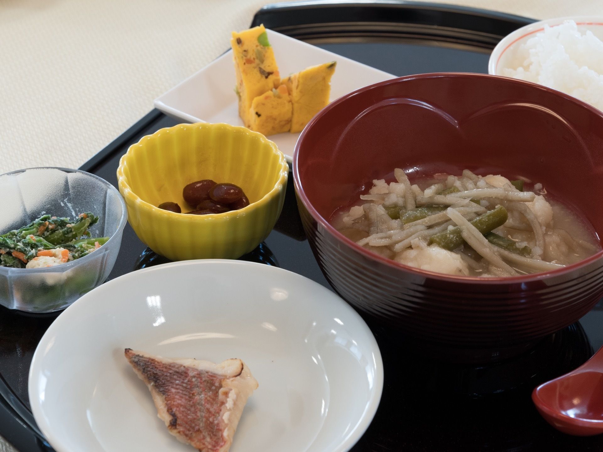黒いプレートに主食、汁物、小鉢ものやデザートが揃えられている。栄養バランスを考慮された、ある日の一食である。