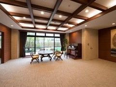 白地に黒い梁が交差した天井、奥に窓があり、テーブルと椅子が置かれたラウンジ