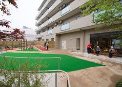 右にベージュの建物があり、その左下に人工芝に手すりの付いた通路が設けられている中庭