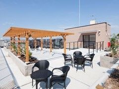 左に日よけの屋根があり、手前に黒い椅子が並べられたテラス