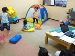ベージュの壁にライトブラウンの床に小さなテントや遊具が並び小さな子どもが遊んでいるスペース