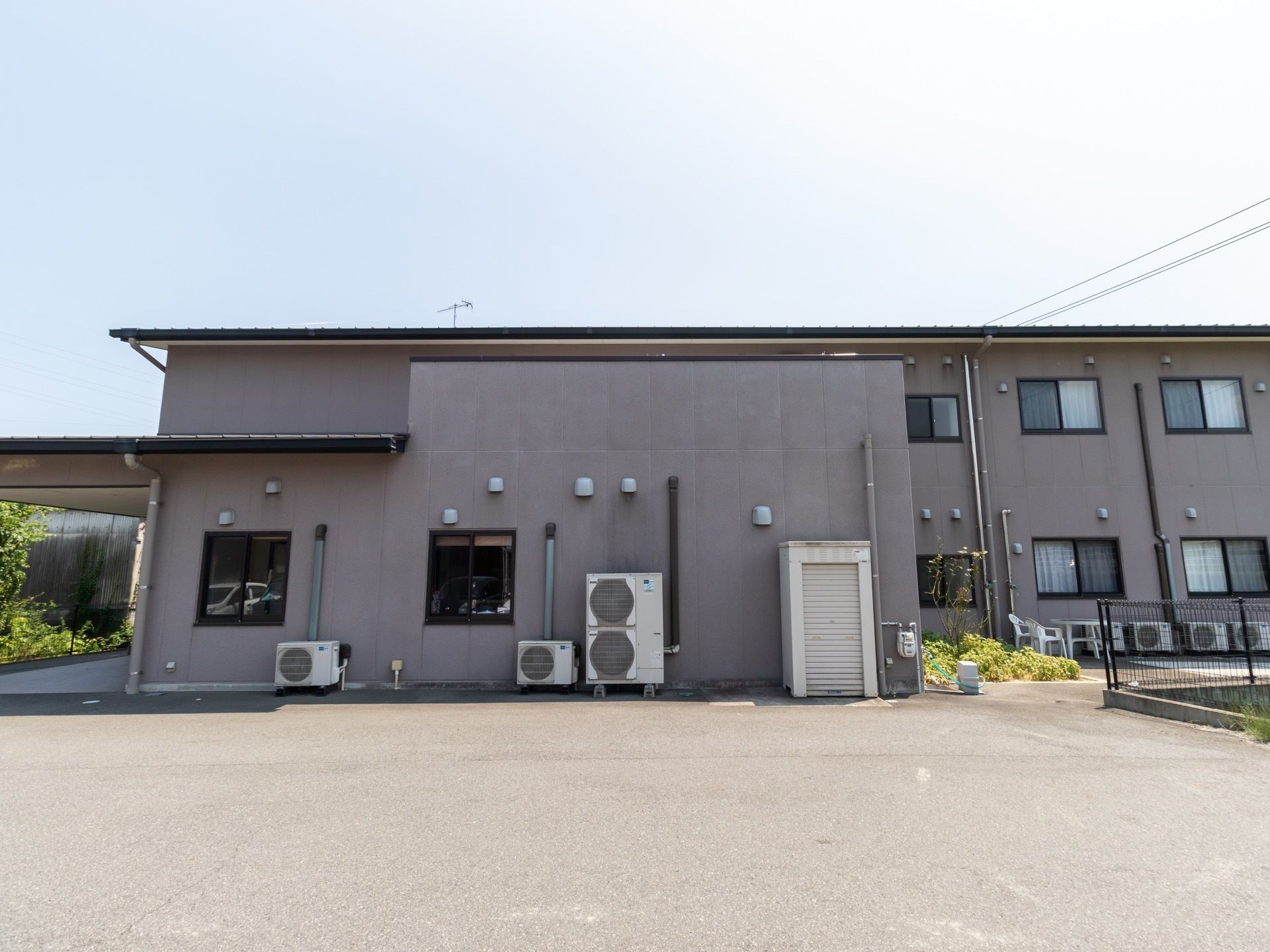 ２階建ての建物があり、窓が規則的に並んで設置されている。また、エアコンの室外機が複数置かれ物置もある。