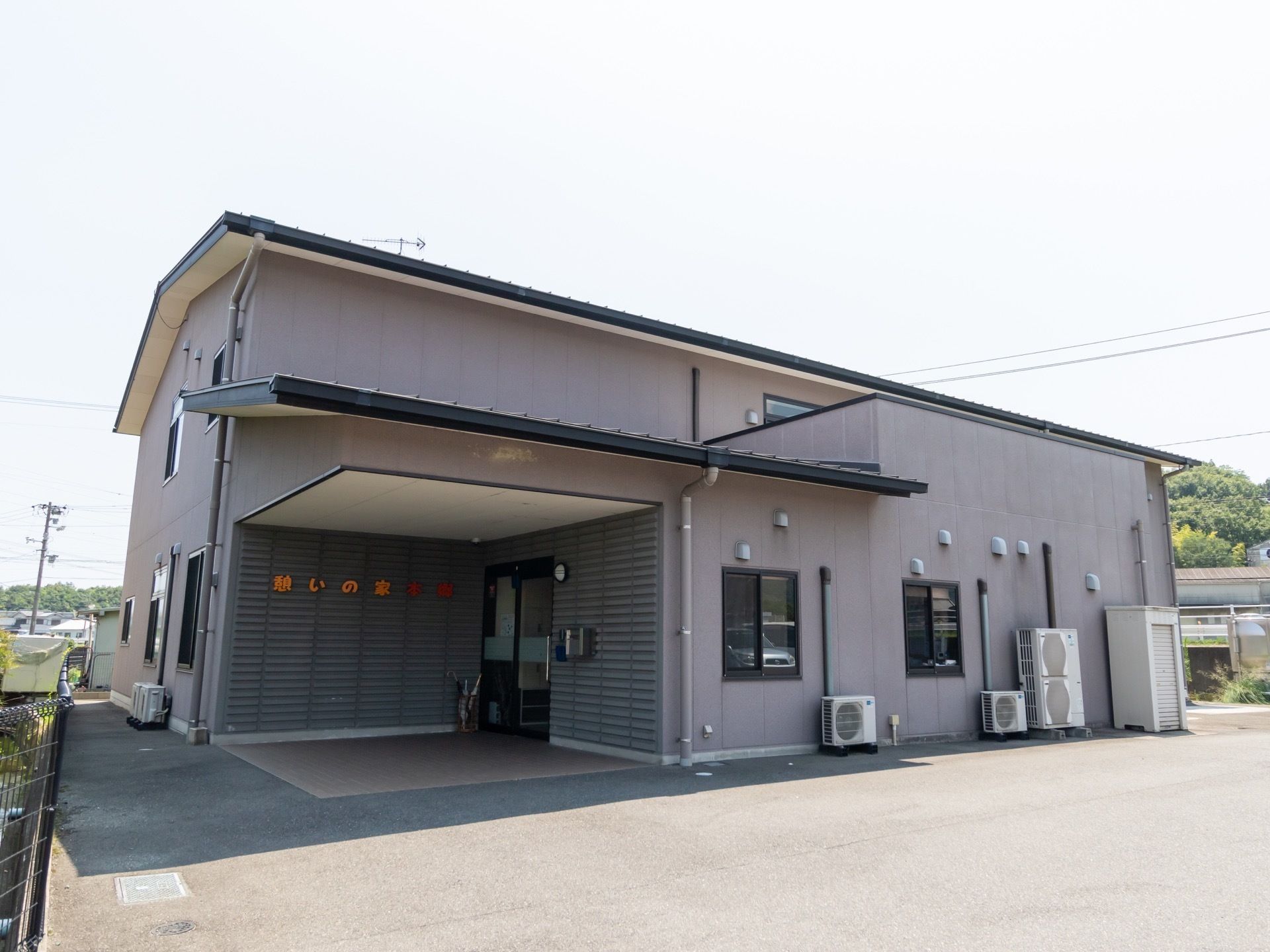 グレーの外壁の２階建ての建物である。周囲には黒い鉄製のフェンスがあり、駐車スペースが確保されている。