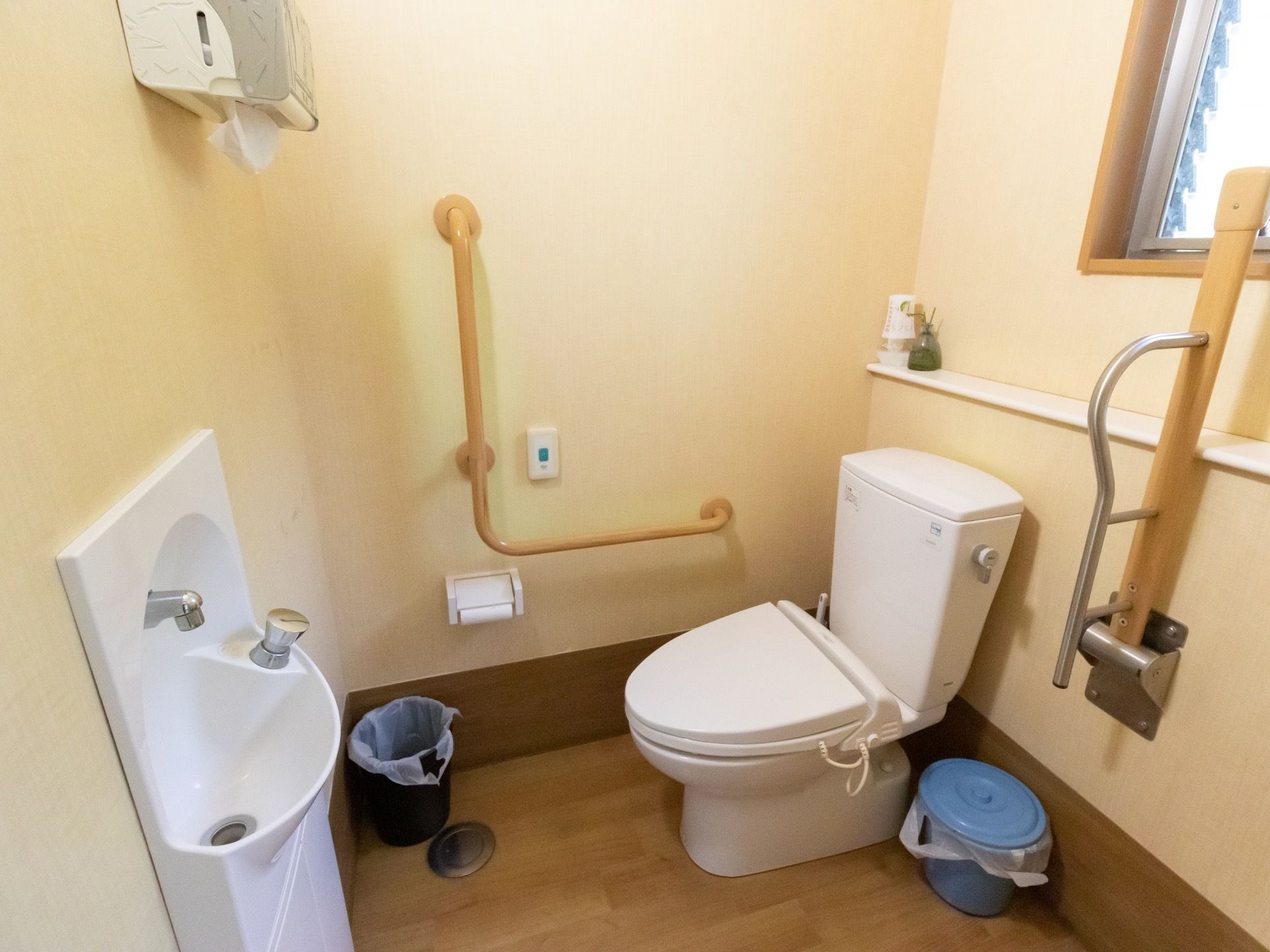 手洗い場と洋式便器の設置されたトイレ。壁には各種の手すりのほか、緊急用の呼び出しボタンが設置されている。