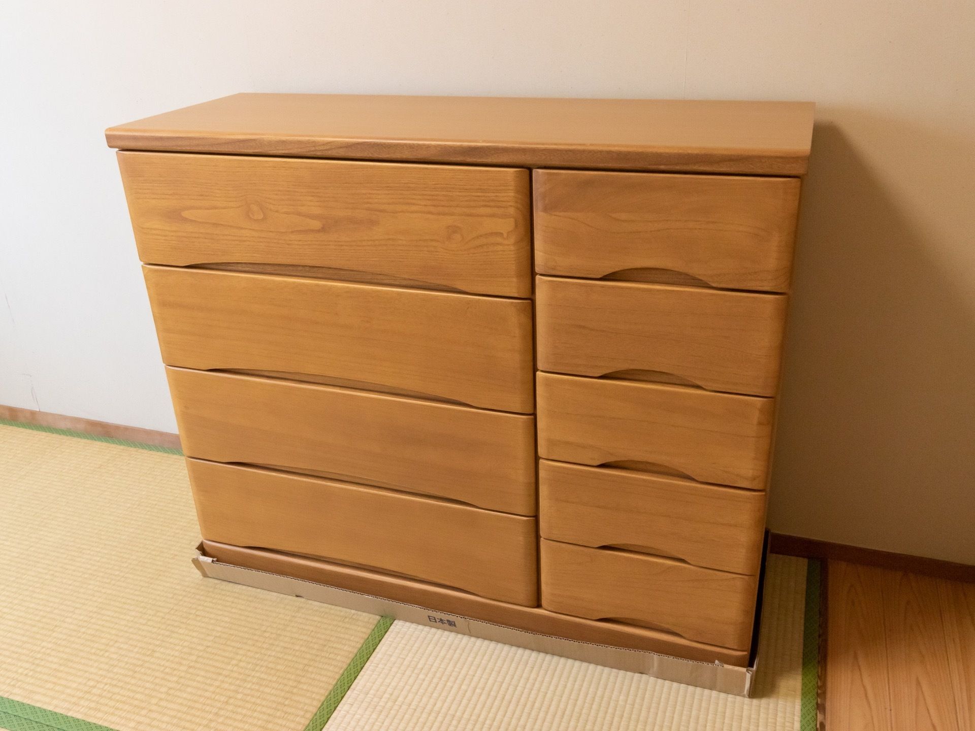 畳の上に木目模様の収納タンスが、１つ置かれている。タンスには大きい引き出しが４つと、小さい引き出しが５つ付いている。