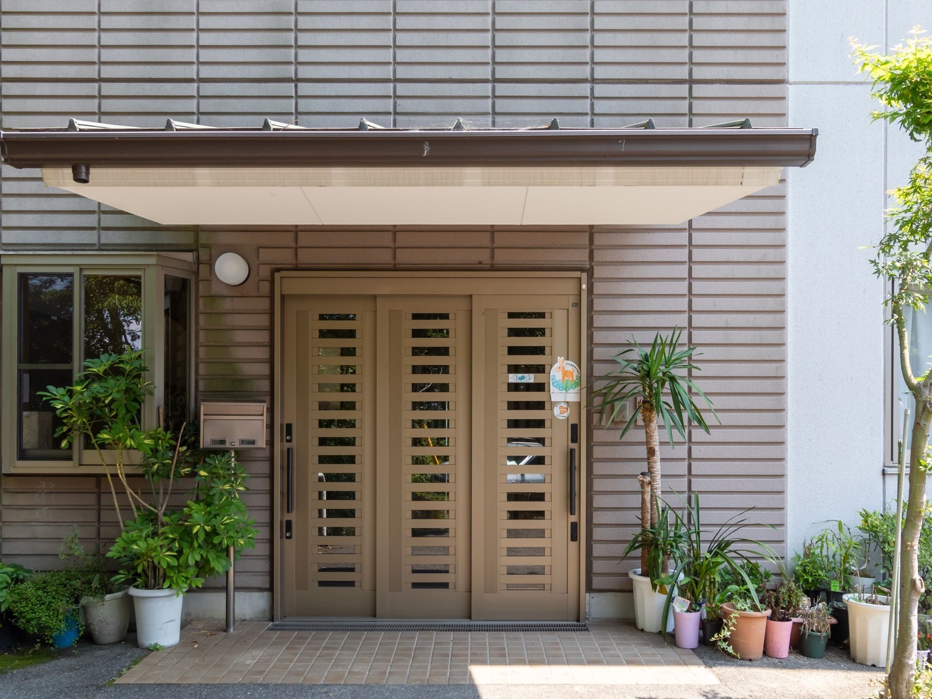 引き戸が採用された玄関。玄関の上にはひさしがあり、周囲には、植物の植えられた鉢が多数並べられている。