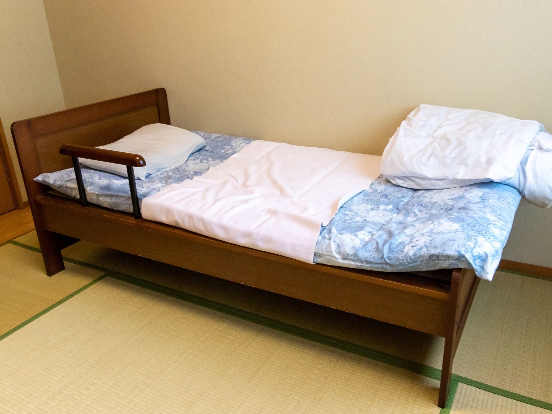 畳敷きの部屋に、和風のデザインの手すり付きベッドが設置されている。ベッドの上には、布団と枕などが置かれている。