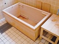 檜風呂の浴槽である。そばにシャワーベンチが置かれており、足腰に不安のある方はシャワーベンチを利用して入浴していただくことができる。