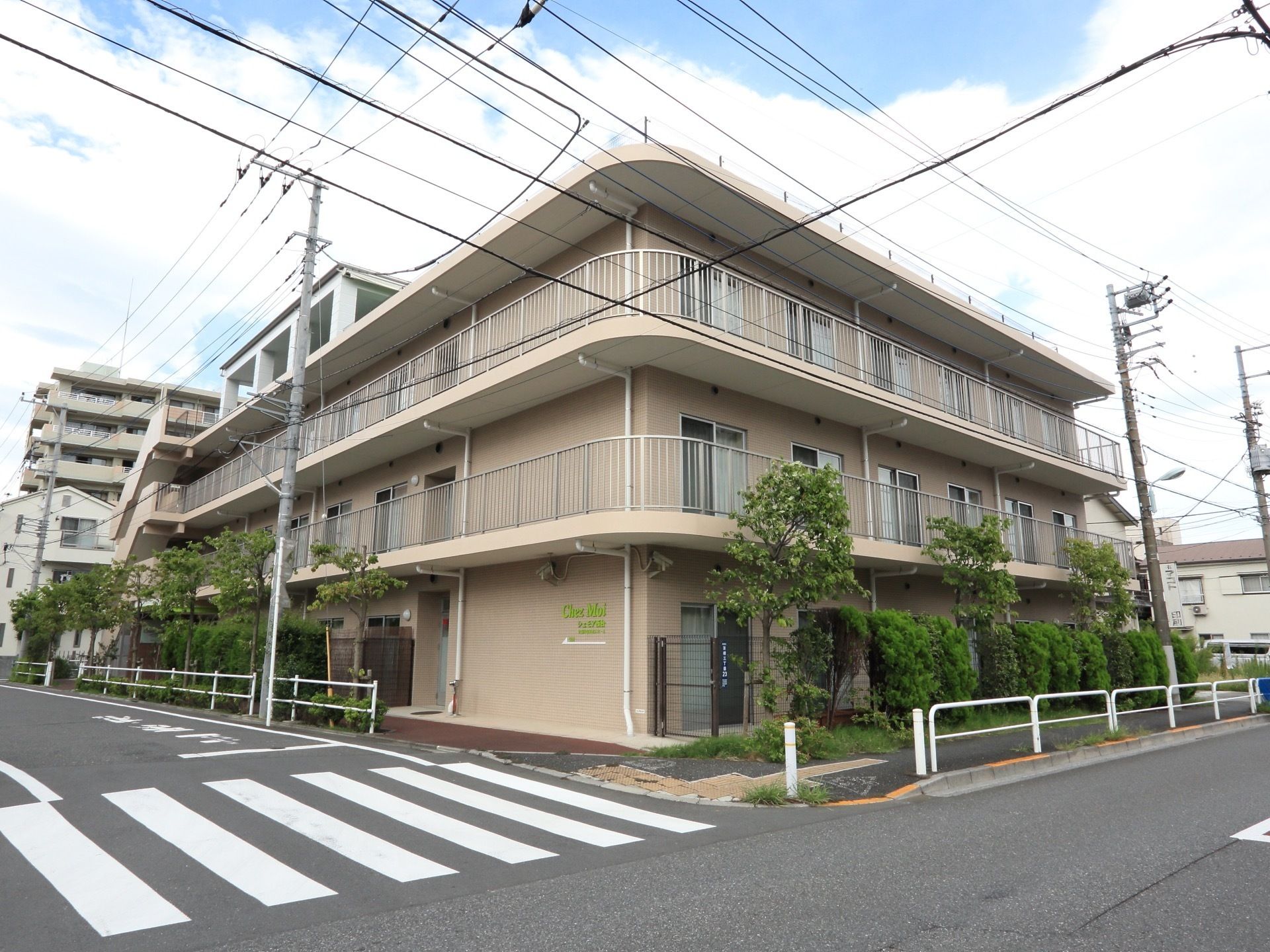 建物は薄いブラウンのカラーで、道路の角地に立地している。また、建物には涼し気な緑のカーテンが掛けられている。