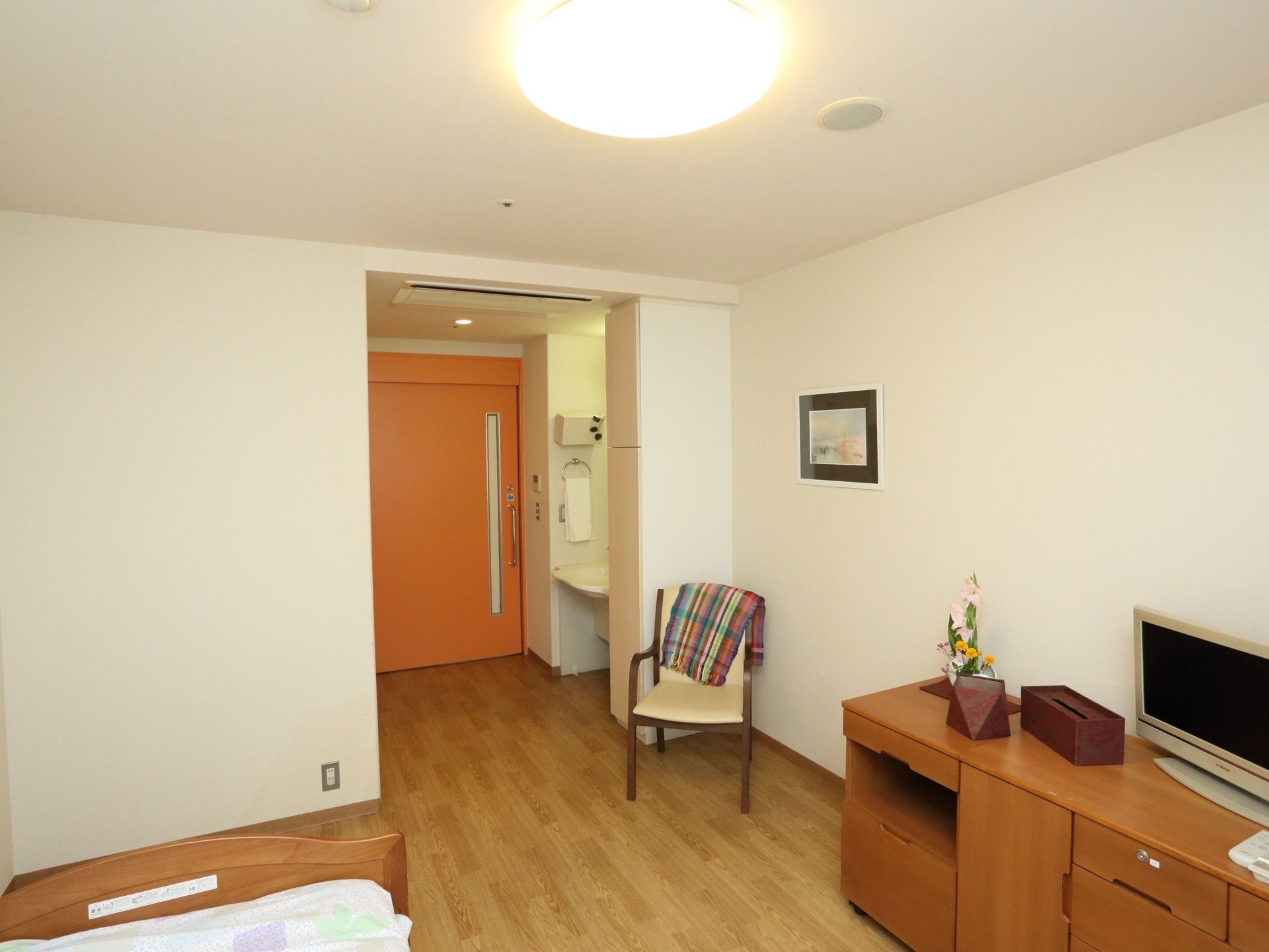 居室入口は大きなスライドドアを採用している。部屋には、ベッド、椅子、棚、洗面台、テレビが完備されている。