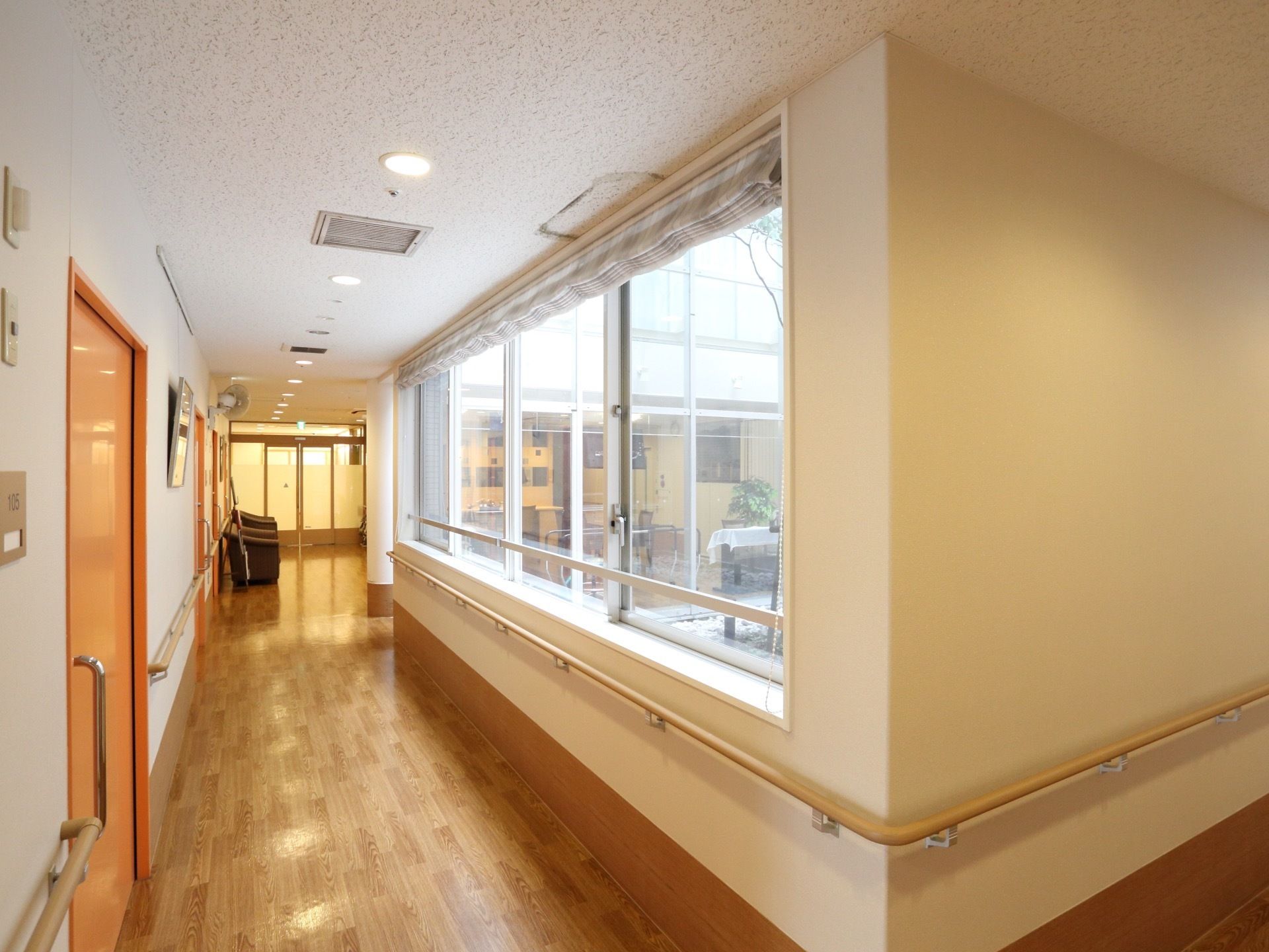 外から明るい日差しが差し込む明るい廊下になっている。部屋のドアはスライド式を採用している。壁には手すりを設置している。