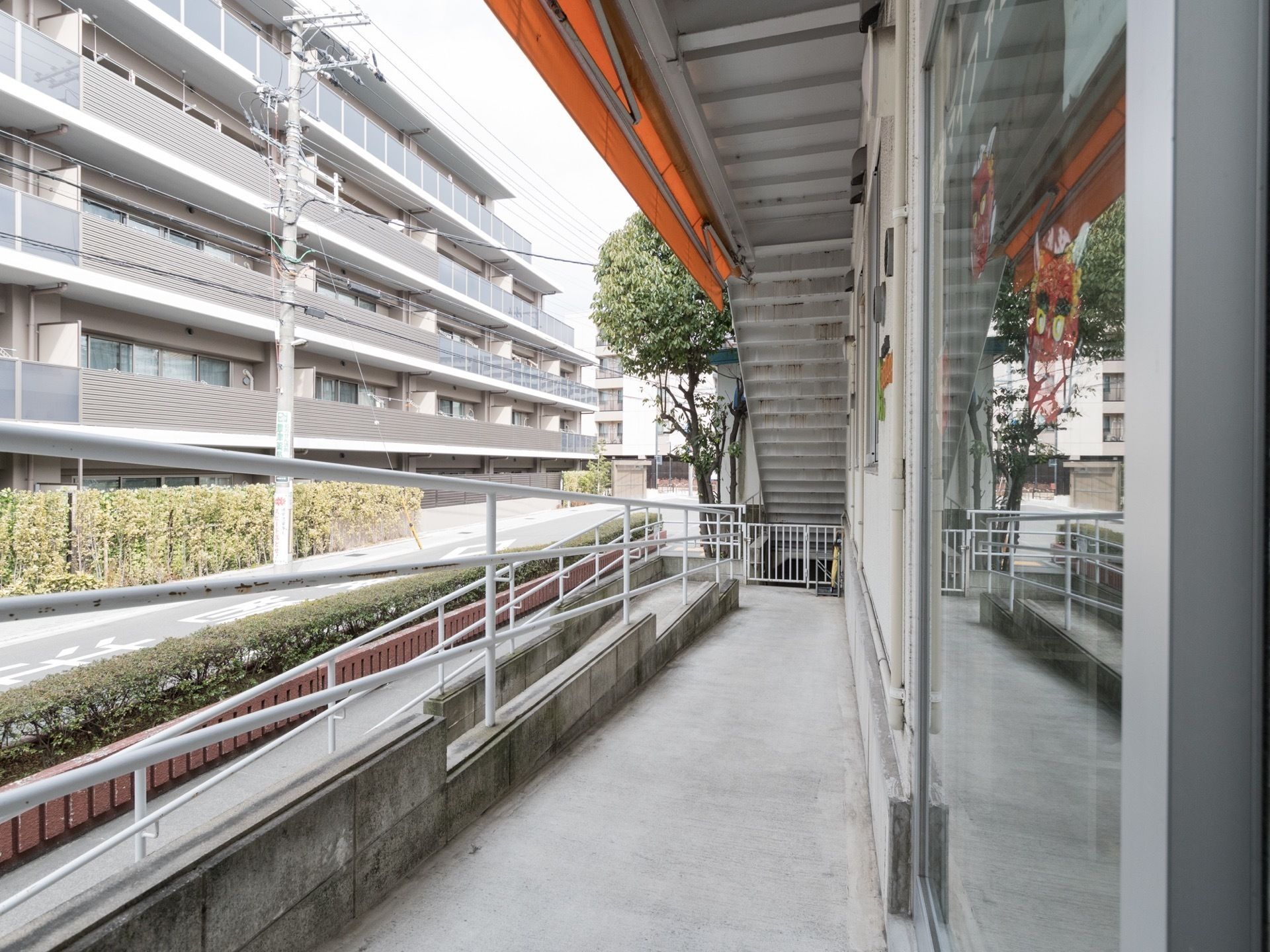 施設の前には大きなマンションが建っている。植え込みの近くには手すり付きのスロープが設置されている。入口扉はガラスである。