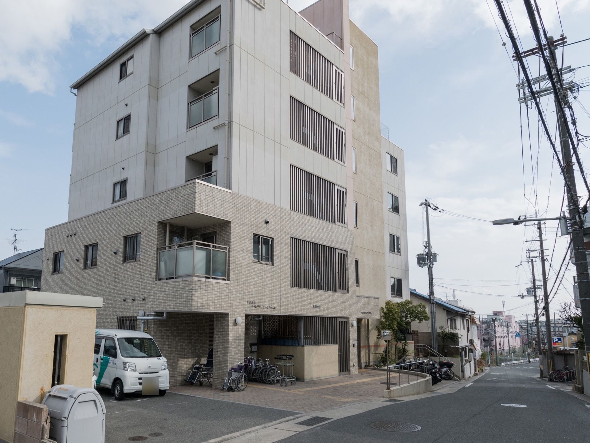 敷地内に車椅子を置くスペースや、駐輪場があるのが見える。建物は閑静な住宅街にあり、落ち着いた雰囲気である。