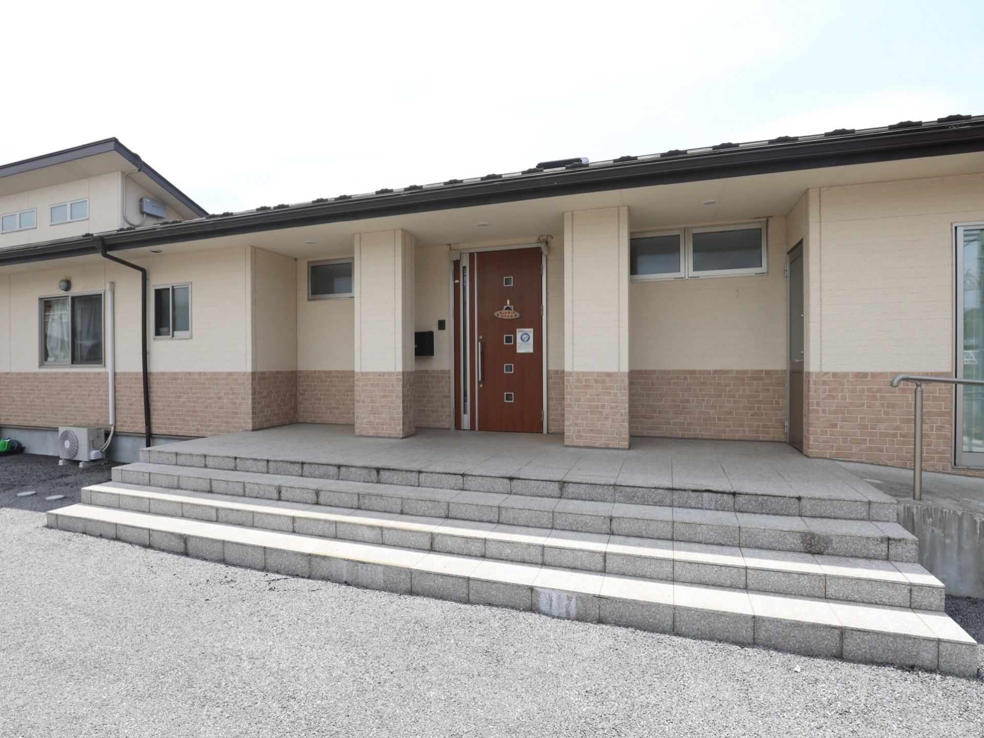 薄いベージュが基調になった外壁の２階建ての建物である。玄関の扉はダークブラウンで、落ち着いた府に気になっている。