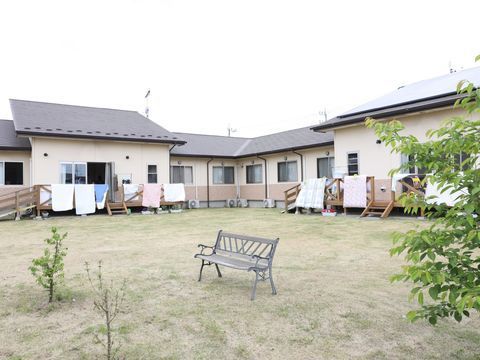 ベージュの壁にグレーの屋根のL字型の建物の手前に広がるベンチの置かれた庭