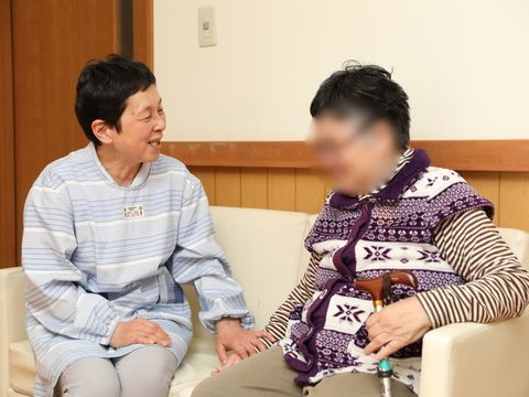 白いソファに座り、手を取りながら会話する2人の高齢女性