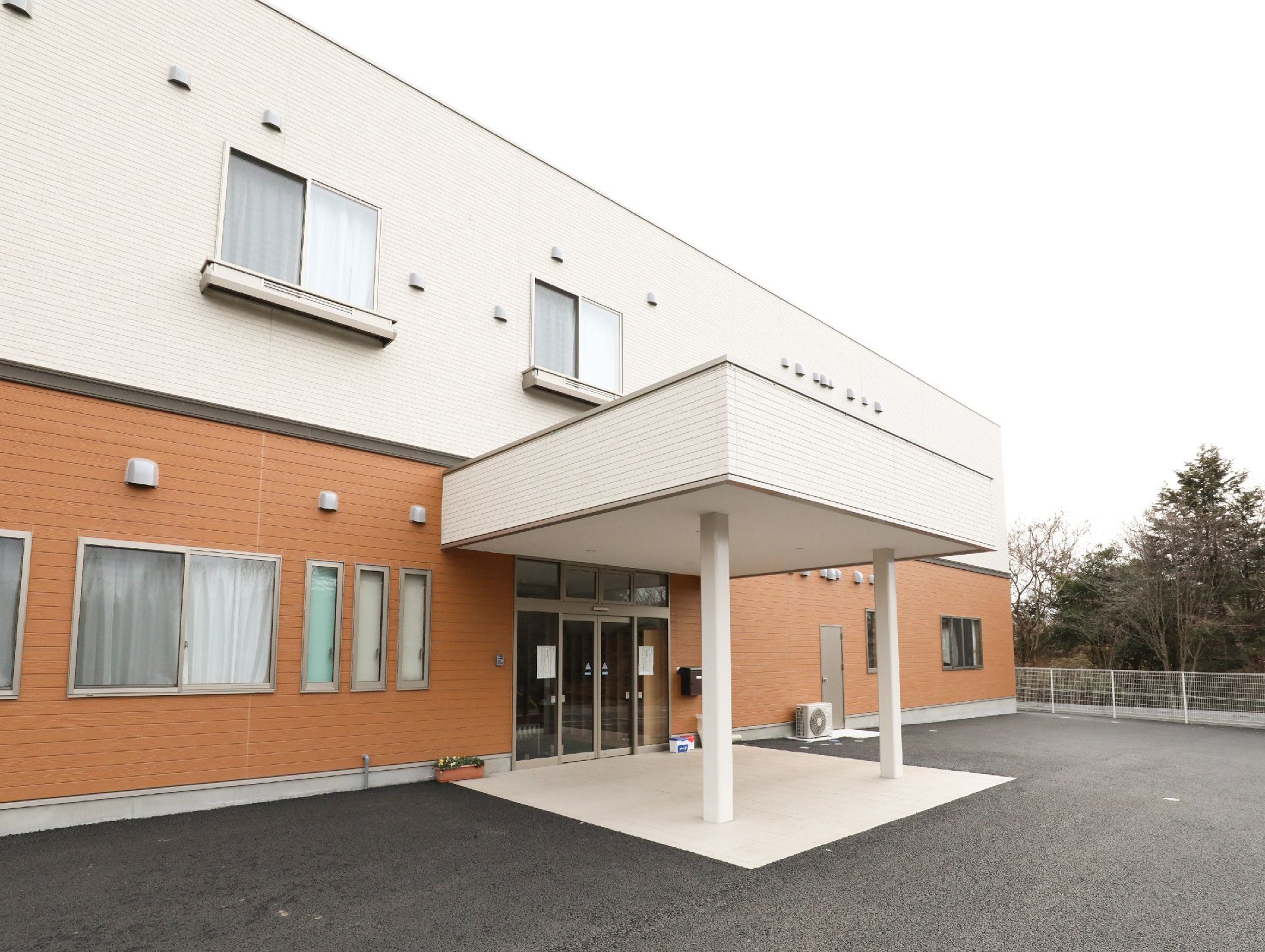 1階はオレンジ2階は白に切り替えた壁面、中央に大きなひさしの付いた玄関のある建物