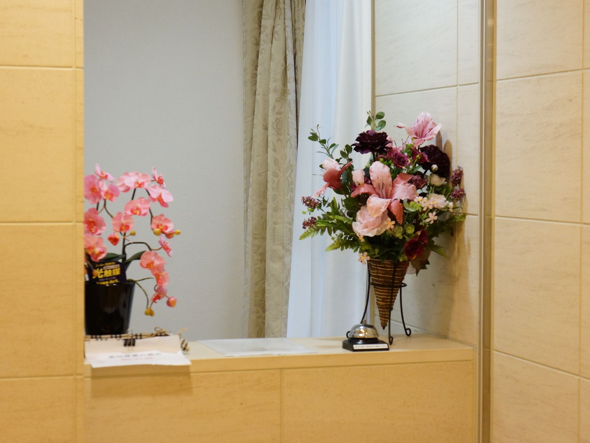 カウンターの上には胡蝶蘭の形をした光触媒の花と百合を中心にした造花がある。。メモ紙と呼び鈴がある。壁はタイル調になっている。
