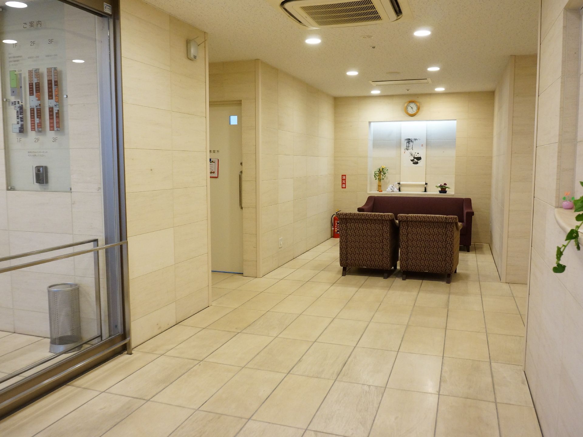 床と壁はタイル調になっていてブラウンのソファーが置いてある。奥には掛け軸があり、全体的にシックな色合いになっている。
