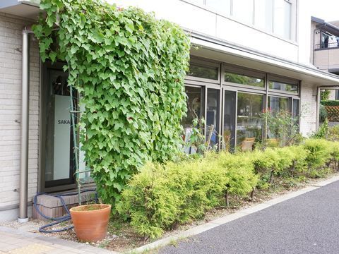 左手前にグリーンカーテンが設けられ、右に向かって植え込みが伸びる大きな窓のある外観