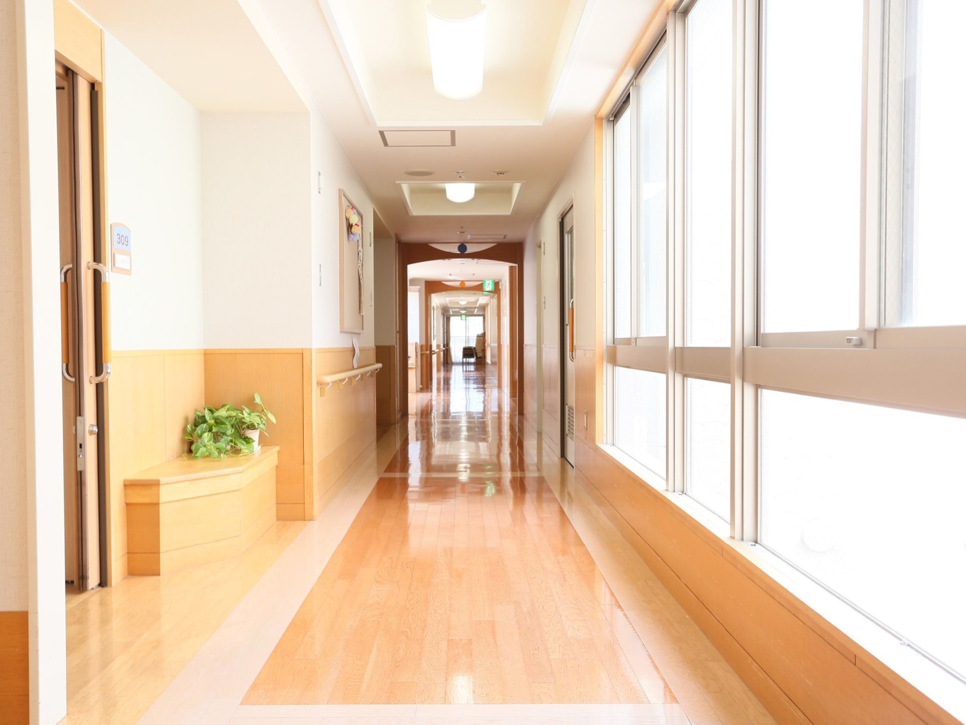 大きな窓があり、日当たりが良い明るい廊下になっている。居室側の廊下の壁には、手すりが備えつけられており、扉の脇にはベンチがある。