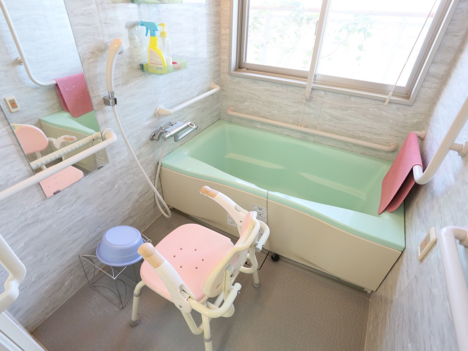浴室内の壁には、手すりが張り巡らされている。浴槽側には、大きな窓があり浴室を明るく演出している。背もたれのある洗体椅子がある。