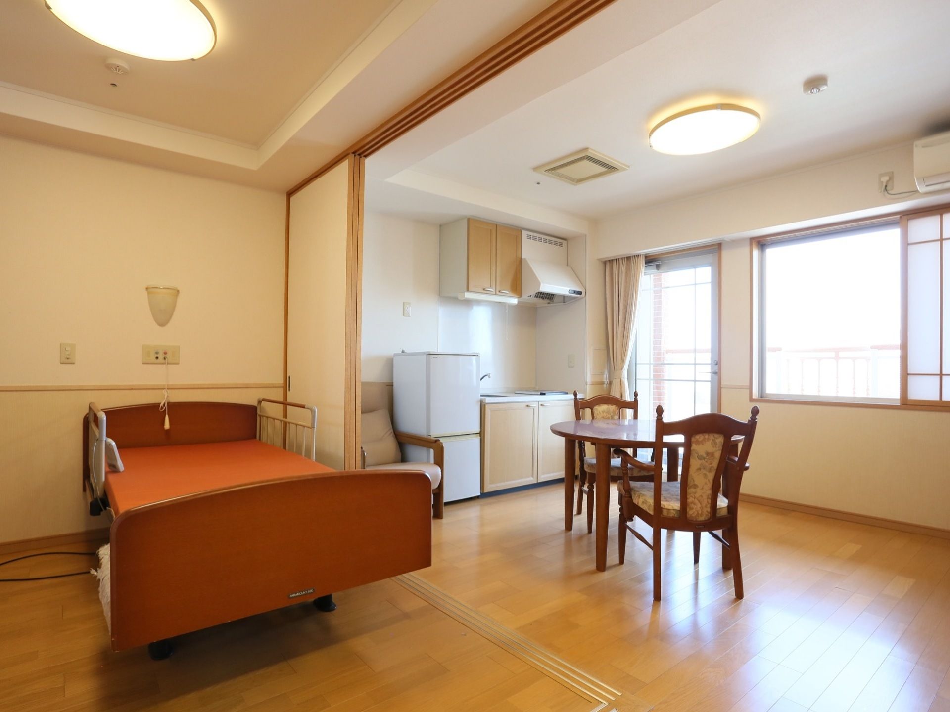 フローリングの個室には介護用ベッドが置かれており、椅子とテーブルのセットも備わっている。部屋にはミニキッチンも設置されている。
