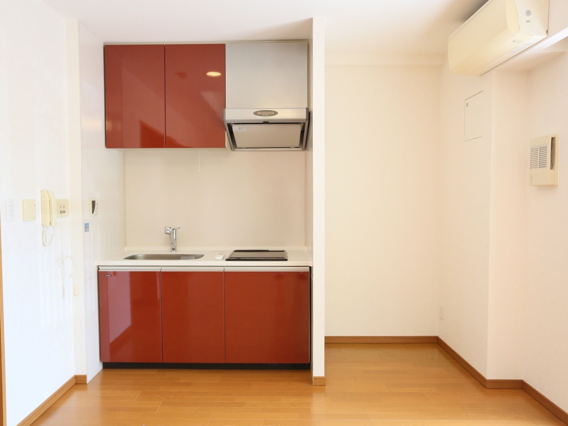 ワイン色のシステムキッチンを完備している。上下には食器や調理器具などを保管できる、収納スペースがある。