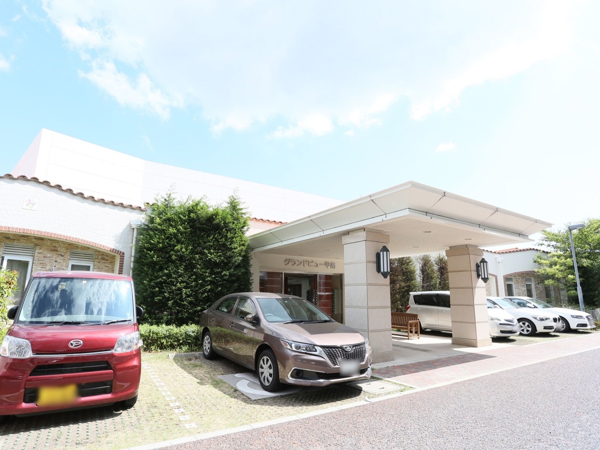 広々とした屋根が備えつけられた、エントランスがある。両脇には、きれいに整備された駐車場が完備されている。