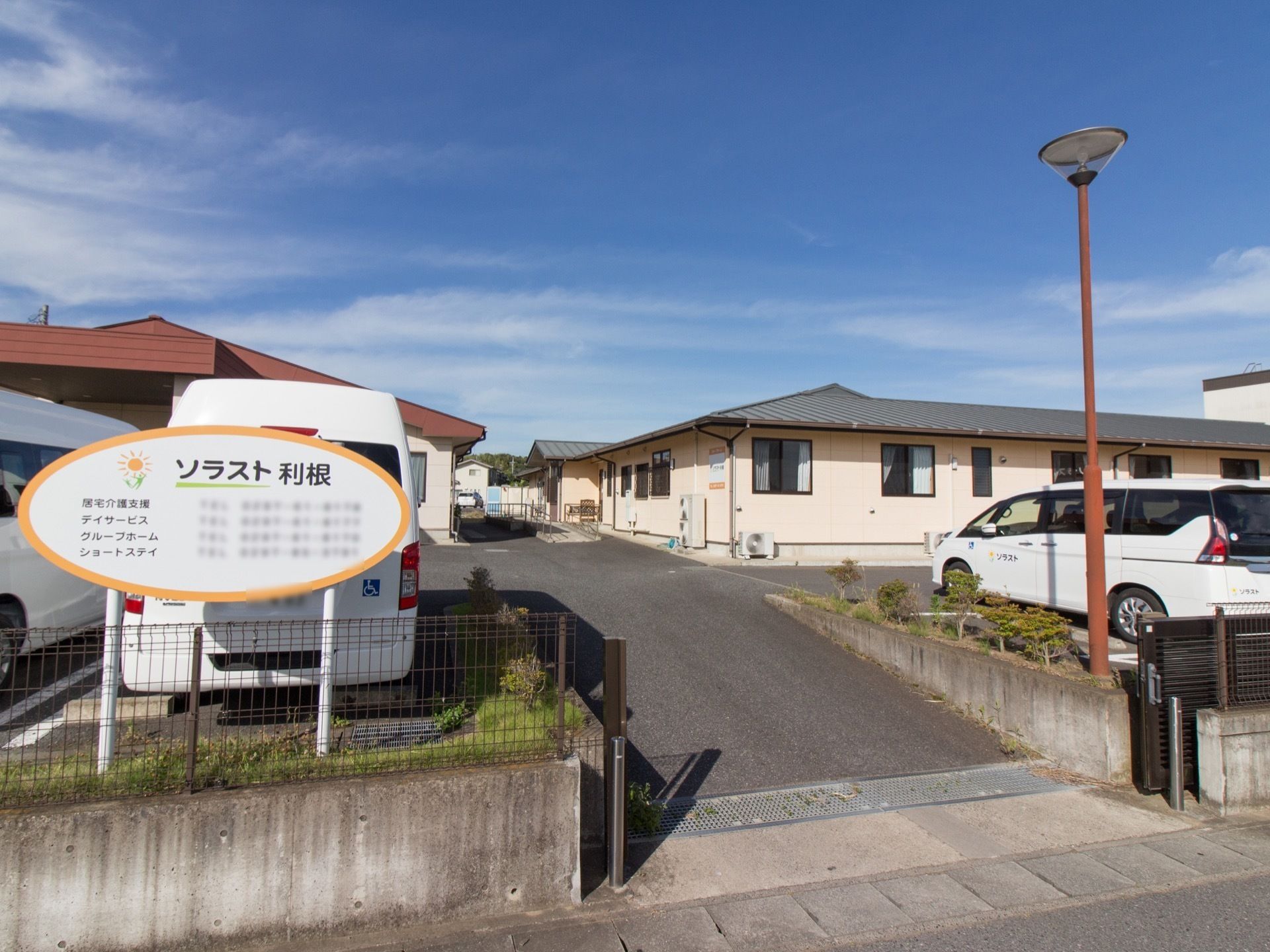 クリーム色の外壁の平屋建ての建物で、敷地内はアスファルトで舗装されている。道路に向かって施設の看板が立っている。