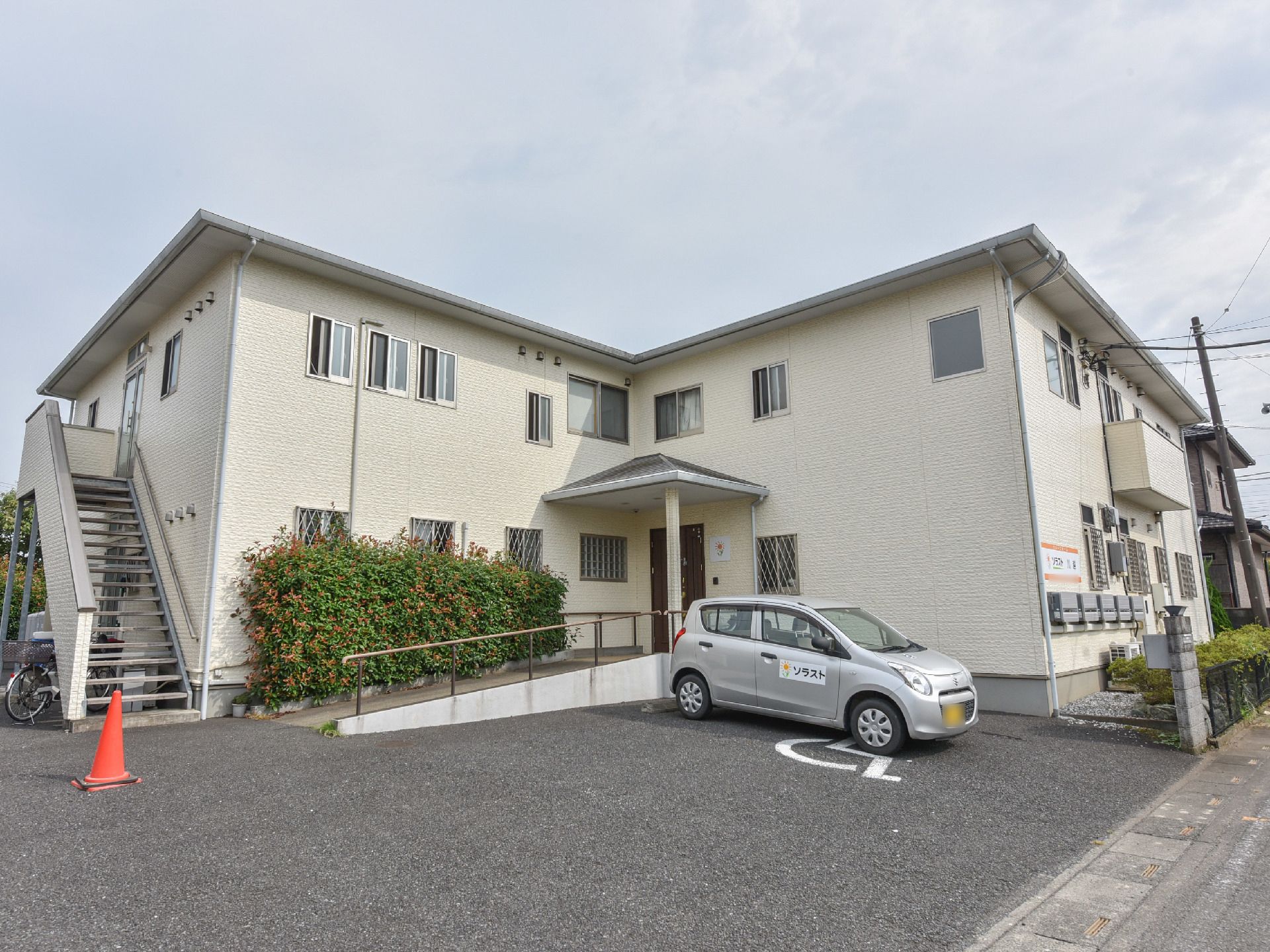 当老人ホームの外観。二階建てで新しい施設となっている。入口には屋根が付いている。また、入口までスロープが続いている。