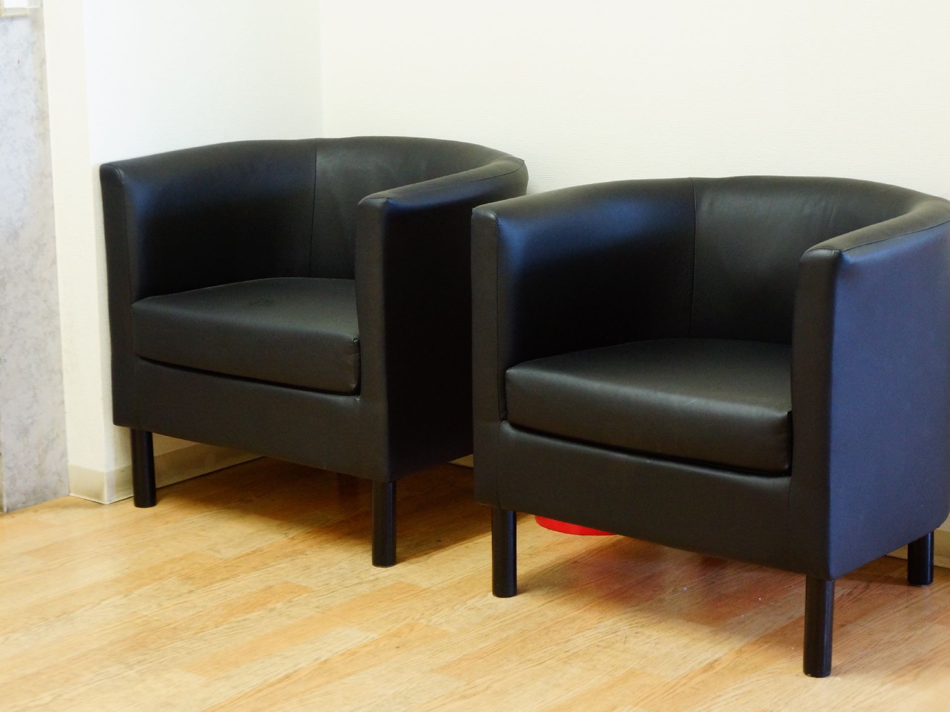 黒い革張りのソファが2台並んでいる。半円形状をしておりフローリングの床の上に白い壁紙を背にして置かれている。