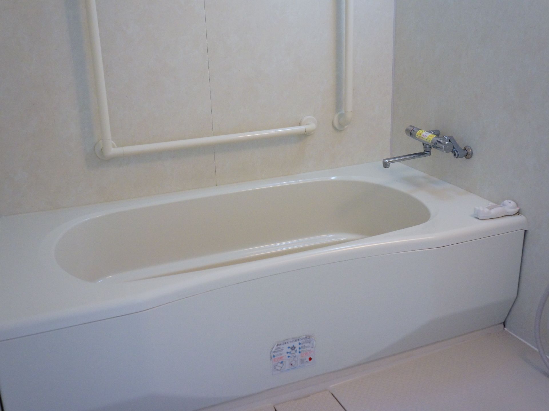 白い浴槽が奥に設置されており、奥にはL字型と垂直、手前には水平の手すりが設置されている。バスタブに対して水栓もついている。