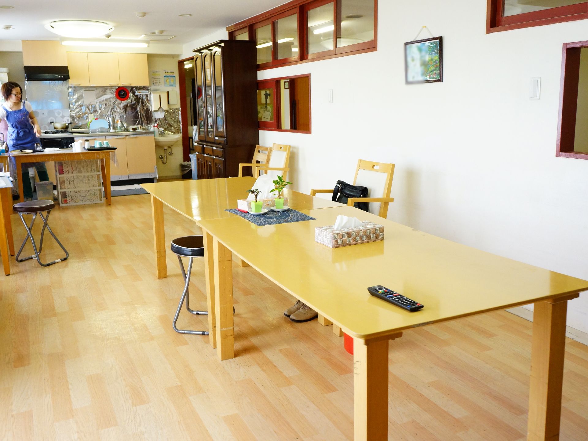 木目調のテーブルが2台並んでフローリングの床の上に置かれています。部屋の一番奥にはキッチンも見えます。