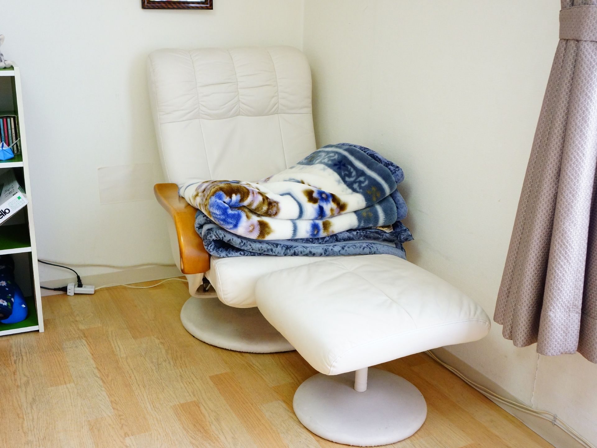 部屋の角に寄せられて白いオットマン付きのソファが置かれている。毛布やブランケットも置かれており右側が窓になっている。